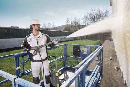 Person using a high-pressure washer on an outdoor platform with a building in the background.